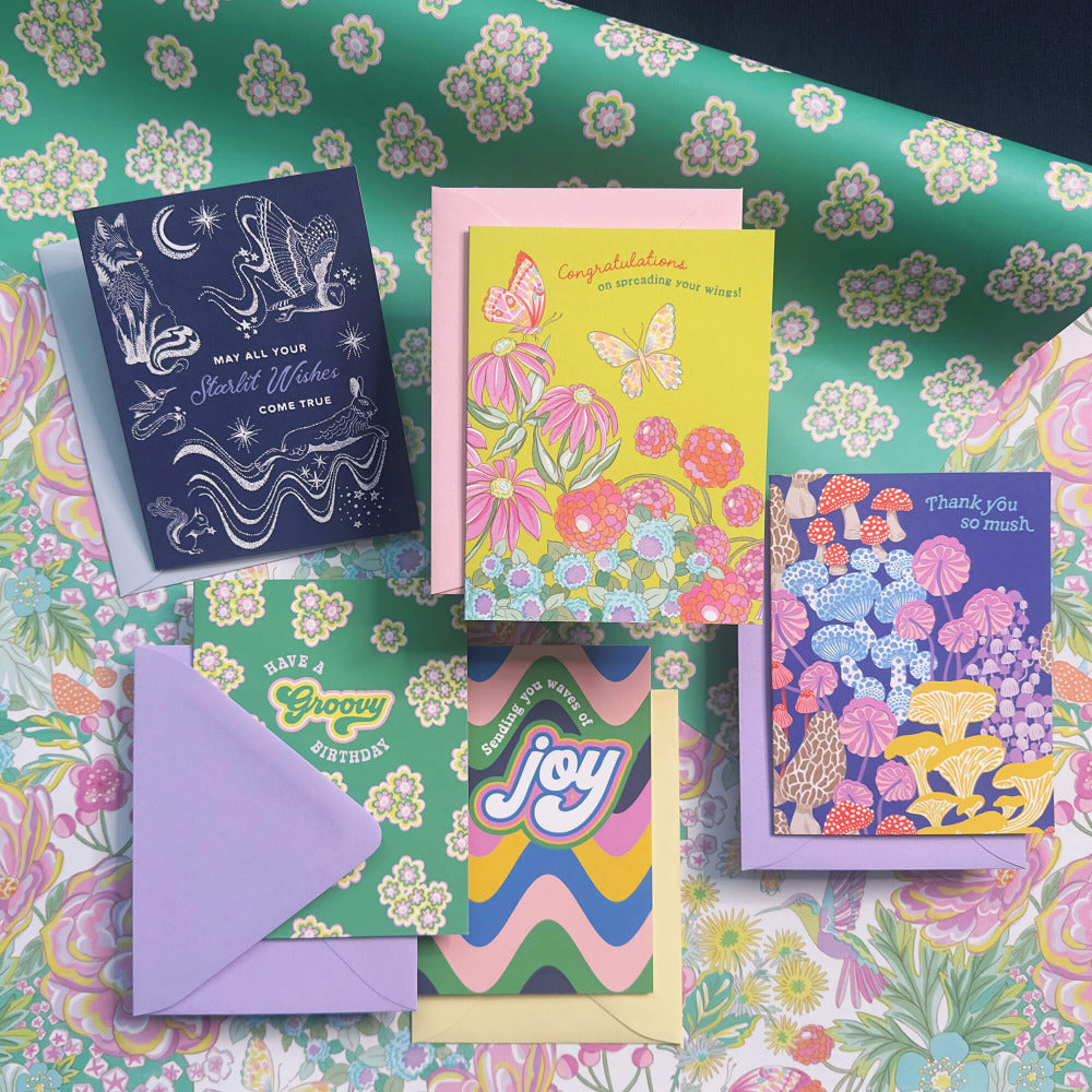 Colorful birthday and thank you greeting cards with envelopes on top of a floral wrapping paper by OOMF Creative